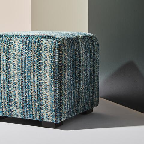 Textured blue and gray ottoman against a neutral wall.