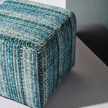 Textured blue and gray cube-shaped ottoman on a neutral background