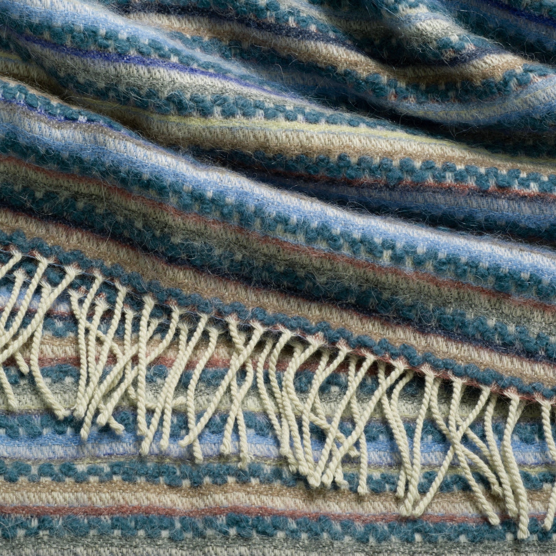 Close-up of a textured fabric with fringes in blue and beige tones.